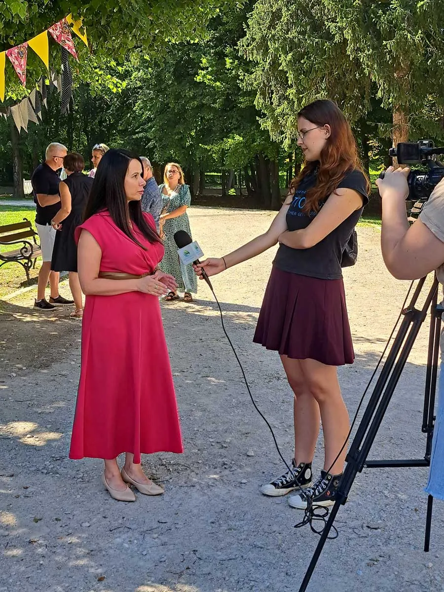 Przedstawicielka PZAZ udziela wywiadu reporterce z mikrofonem, w tle kamera i park