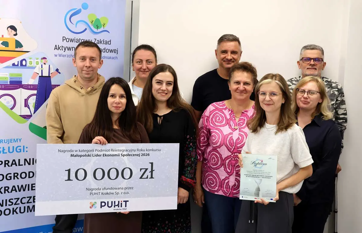 Dziewięcioro pracowników PZAZ przy roll-upie Zakładu z symbolicznym czekiem na 10 000 zł i dyplomem konkursu Małopolski Lider Ekonomii Społecznej 2026